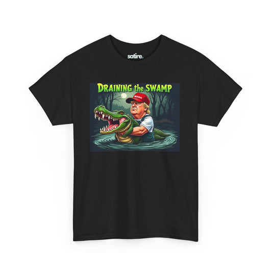 Black t-shirt with a graphic design featuring a cartoon Donald Trump in waders holding a large alligator in a swamp under a full moon, with the text 'DRAINING THE SWAMP' above in bold yellow and green letters. | Satire Clothes