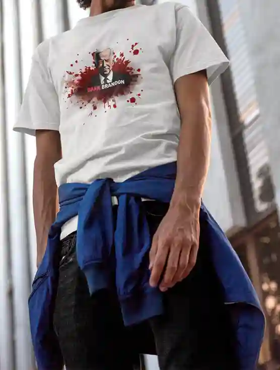 A man wearing a white t-shirt with a graphic of a man with white hair in a suit, surrounded by red splatter effects, and the text 'DARK BRANDON' in bold white and red letters below the image. He has a blue jacket tied around his waist | Satire Clothes