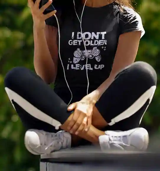 Woman wearing a Black 'I Don't Get Older, I Level Up' T-Shirt with a graphic of a game controller and plus signs | Satire Clothes