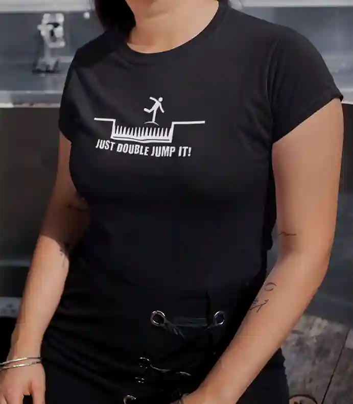 Woman wearing a black t-shirt with a white graphic of a stick figure jumping over spikes and the text 'JUST DOUBLE JUMP IT!' below | Satire Clothes
