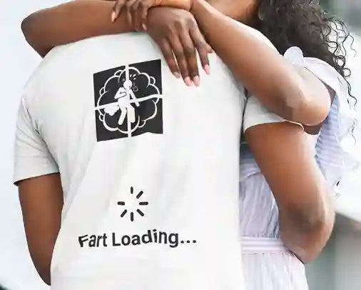 Couple embracing, with the man wearing a white t-shirt featuring a humorous design of a silhouette in a cloud of gas within a crosshair, followed by a loading symbol and the text 'Fart Loading...' | Satire Clothes