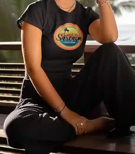 A woman wearing a black t-shirt with a colorful circular design featuring a palm tree and the text "Fluent in Sarcasm Life's a Beach" in a playful font. | Satire Clothes