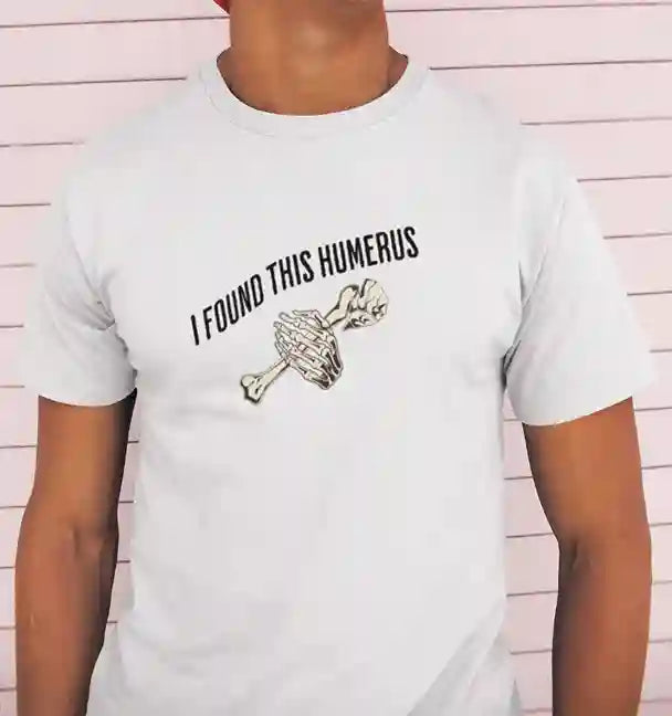 A man wearing a white t-shirt with the text 'I FOUND THIS HUMERUS' printed in black. Below the text, there's an illustration of a skeletal hand holding a humerus bone. | Satire Clothes