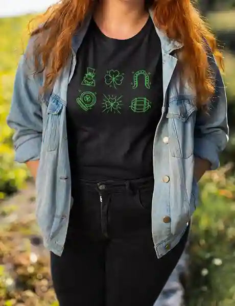 Woman wearing a black tee with green icons of leprechaun, shamrock, horseshoe, sunburst, and barrel | Satire Clothes