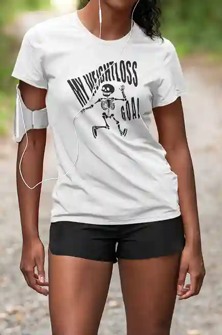 A woman wearing a white t-shirt featuring a humorous black skeleton graphic with the text "MY WEIGHTLOSS GOAL" in a distressed font above it | Satire Clothes