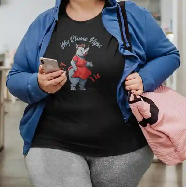 Plus size woman wearing a black t-shirt featuring a cartoon rhinoceros dressed in a red dress with text 'My Rhino Hips' in gray and 'Don't Lie' in red | Satire Clothes