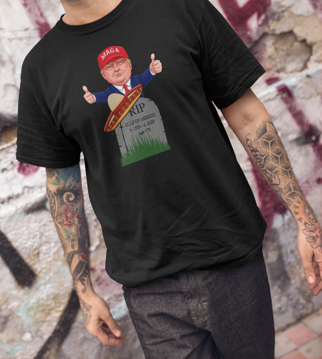 A man wearing a black t-shirt with President Trump in MAGA hat giving thumbs up behind tombstone reading "RIP GULF OF MEXICO b. 1550 - d. 2025" with sombrero | Satire Clothes