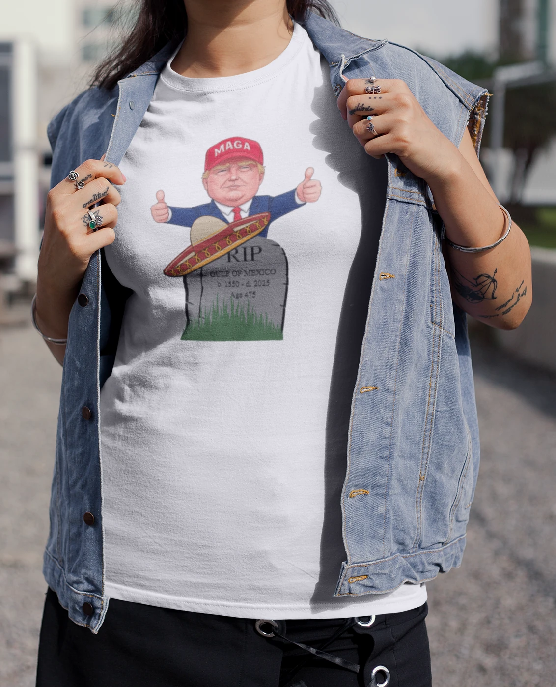 A woman wearing a white t-shirt with President Trump in MAGA hat giving thumbs up behind tombstone reading "RIP GULF OF MEXICO b. 1550 - d. 2025" with sombrero | Satire Clothes