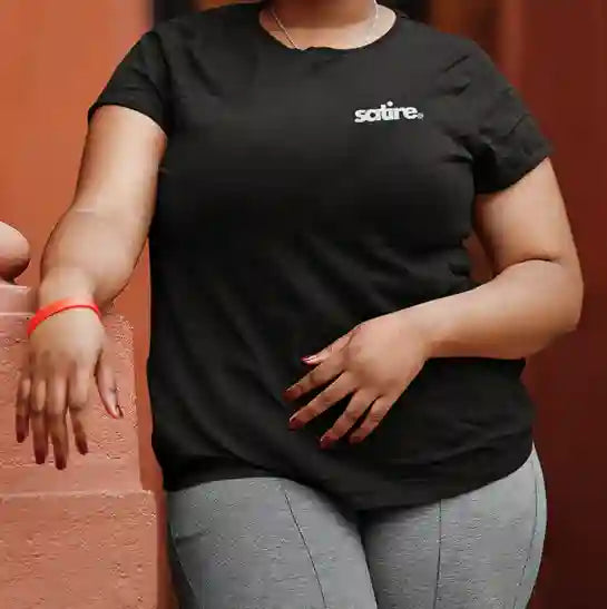 Plus size woman wearing a black t-shirt with the 'Satire.' logo in white and blue text on the left chest area. | Satire Clothes