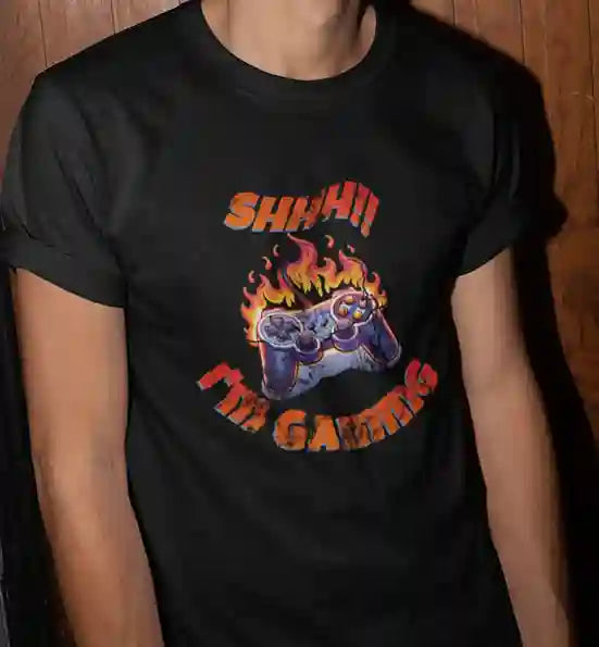 Man wearing a black T-shirt with a graphic of a flaming game controller and the text "SHH!! I'M GAMING" in bold, fiery letters | Satire Clothes