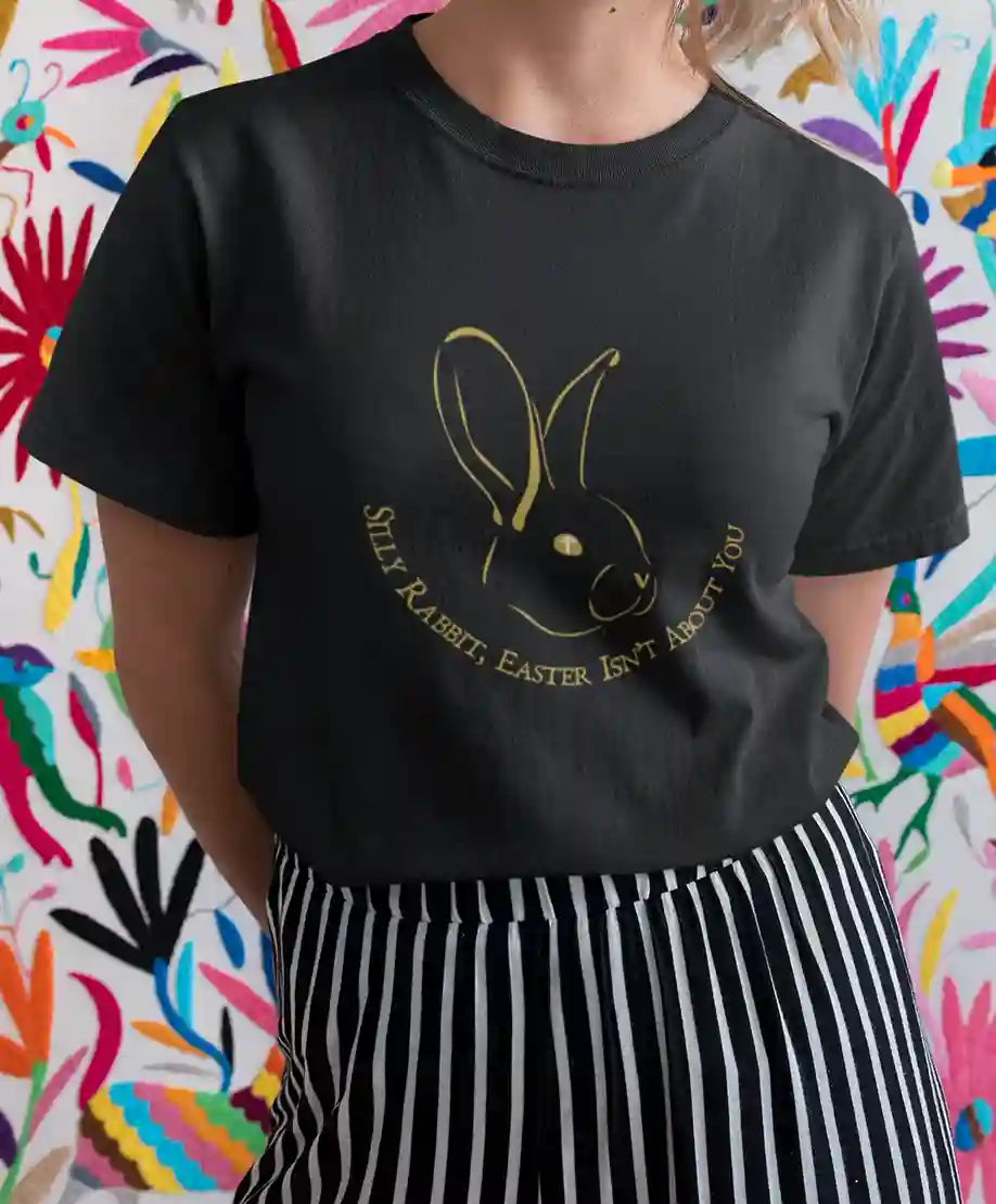 A woman wearing a black t-shirt featuring a satirical bunny graphic with 'Silly Rabbit, Easter Isn't About You' text in gold | Satire Clothes