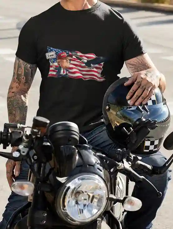 A man wearing a black t-shirt featuring a satirical design of Donald Trump holding an "I WON" sign in front of an American flag with an eagle flying above | Satire Clothes