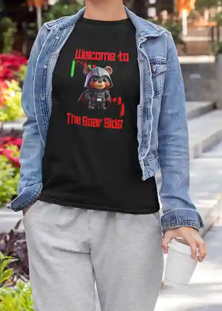 A woman wearing a black T-Shirt with 'Welcome to The Bear Side' text in red, featuring a cute bear wearing a black helmet and uniform with a cape, amidst stock market graphs, symbolizing a humorous take on the bear market. | Satire Clothes