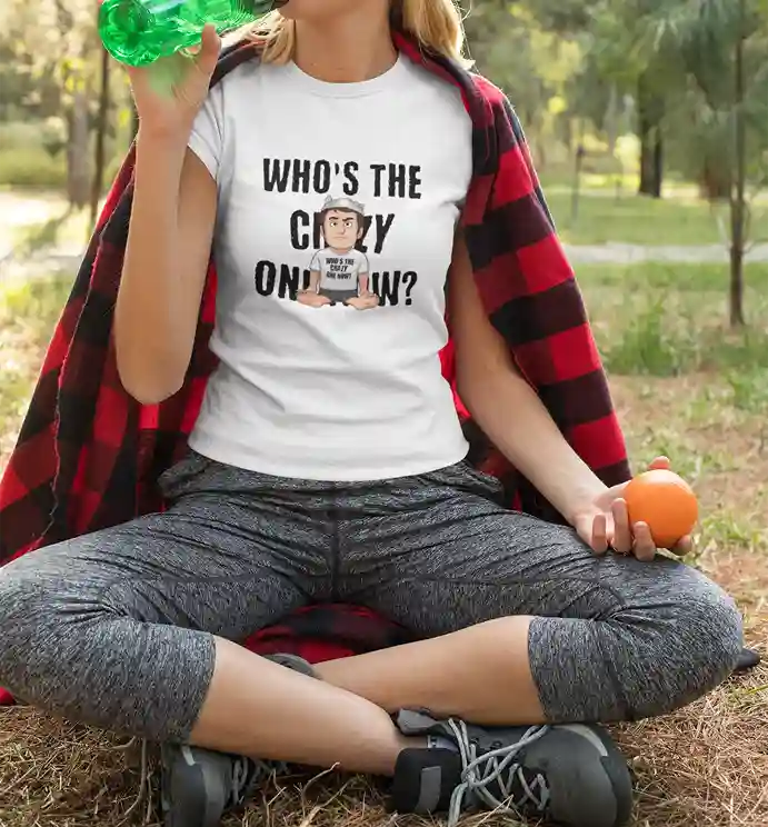 A woman wearing a white t-shirt with the text "WHO'S THE CRAZY ONE NOW?" in bold letters. Overlapping the text, there's a cartoon character wearing a tin foil hat and a shirt that says "WHO'S THE CRAZY ONE NOW?" while sitting cross-legged | Satire Clothes