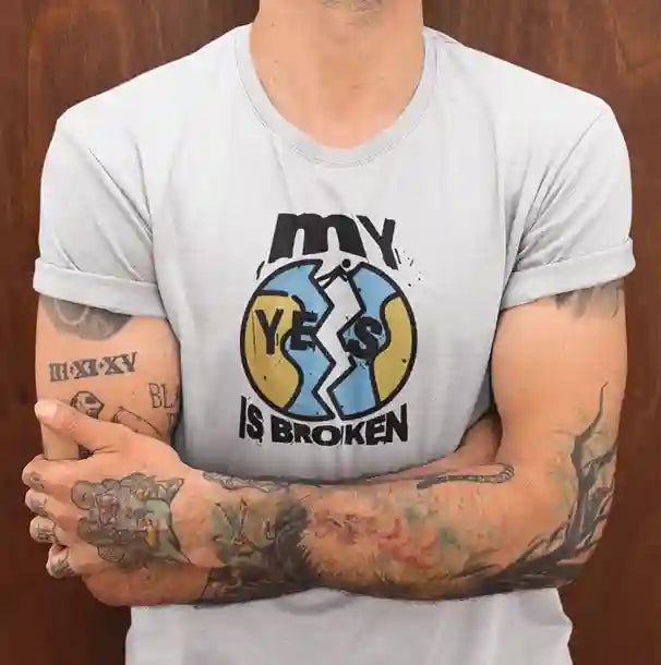 A man wearing a white 'My Yes Is Broken' T-Shirt featuring a cracked 'YES' design in yellow and blue, with bold text above and below | Satire Clothes