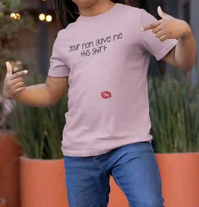 Man wearing a light pink t-shirt with the text "your mom gave me this shirt" printed in black, featuring a red lipstick kiss print at the bottom | Satire Clothes